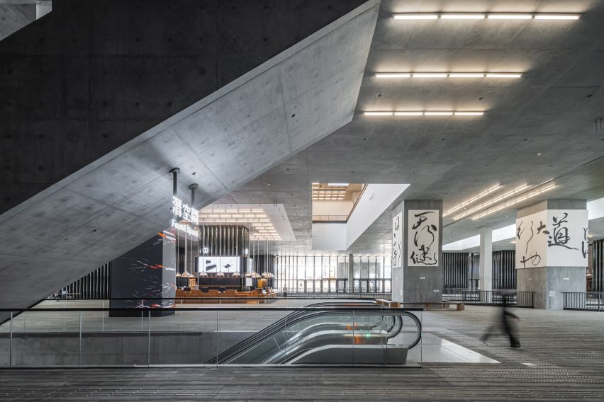 Main Hall of the M+ Museum with slanted concrete truss hanging over the space and an escalator leading downstairs