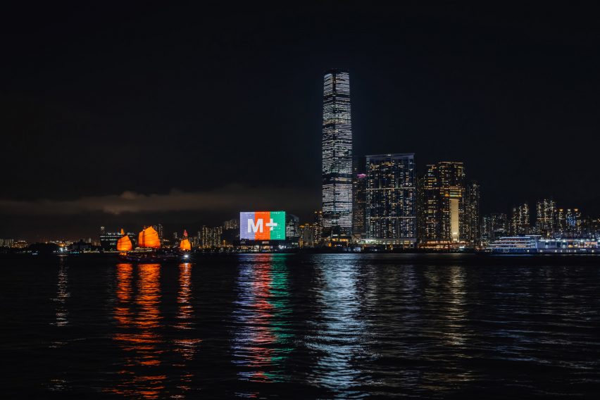 M+ museum with its facade illuminated at nighttime with the light reflecting on Victoria Harbour