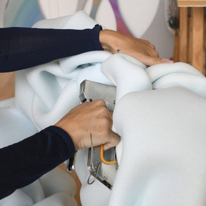 Woman stapling light blue upholstery onto a chair for Massproductions' Face Lift network
