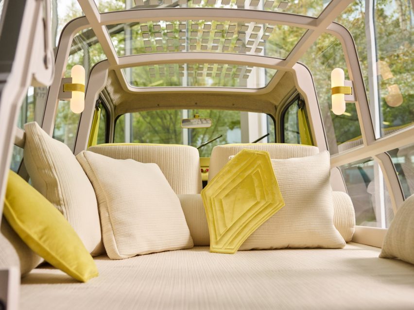 Bed in the boot of the Renault Suite No.4 with cream chenille upholstery, cushions and wraparound transparent panelling showing views of a forest