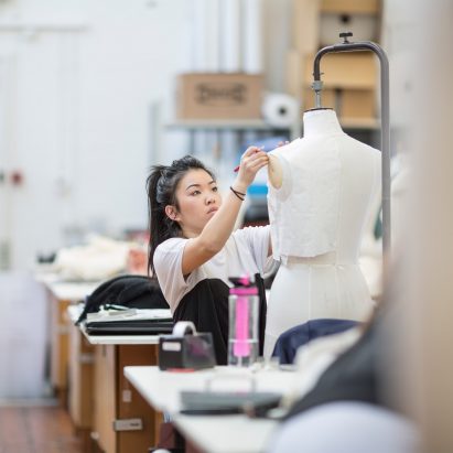 A photograph of a student pinning fabric to a dressmakers' mannequin