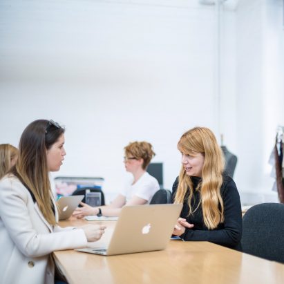 Students sit around a work bench in a studio