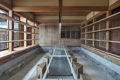 Workspace with sunken concrete floor and long glass table by DDAA Inc
