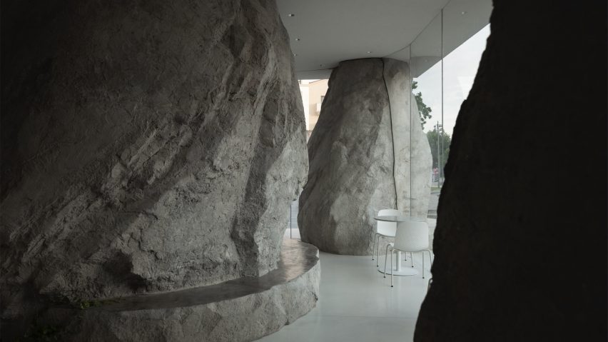 Boulder-like columns surround white chairs and tables in Zolaism Café in Aranya designed by B.L.U.E. Architecture Studio