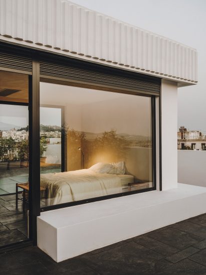 Bedroom of 10AM Lofts penthouse in Athens with two glass walls and a simple white bed without a headboard