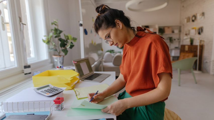 Student with hair tied in a bun and wearing glasses making notes at a desk