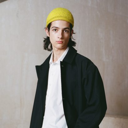 Man wearing a yellow crochet hat, white shite and black jacket from collaboration between Fibershed and Phoebe English for COP26