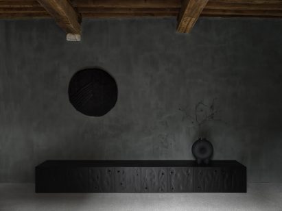 Low black cabinet and black wall hanging in black-painted room at Faina Gallery in Antwerp