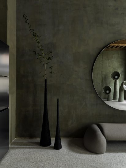Two triangular black vases in front of green wall in showroom by Yakusha Design