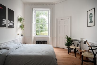 Bedroom of Edinburgh apartment Luke McClelland with plain grey bread spread and wicker armchairs next to a low sidetable 
