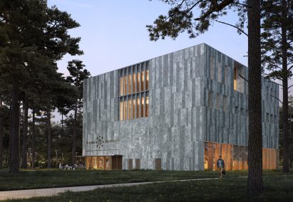 Exterior of the Tilburg University Lecture Hall at dusk, showing warm light shining through narrow vertical apertures in the grey stone facade