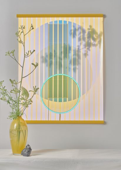 Ra tapestry pictured at daytime hung behind a vase with flowers