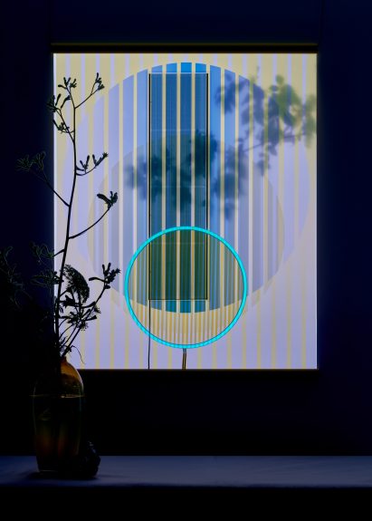Solar tapestry by Marjan van Aubel pictured at nighttime hung behind a vase with flowers with a glowing blue ring at its centre