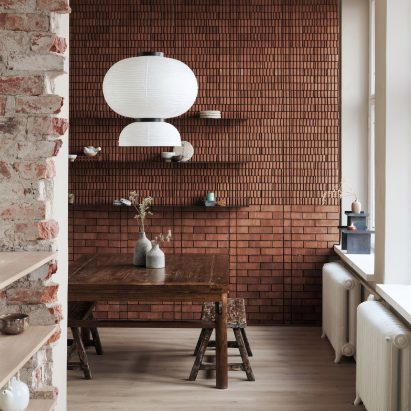 Tea tasting room with red brick wall and paper lantern above weathered wooden table in Teemaa teahouse in Helsinki, designed by Yatofu