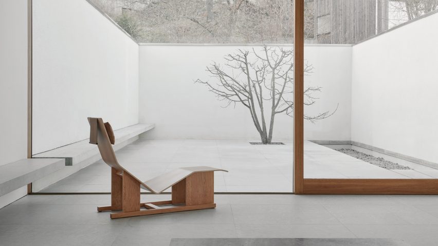 Wooden chaise lounge by Massproductions in front of a large glass sliding door