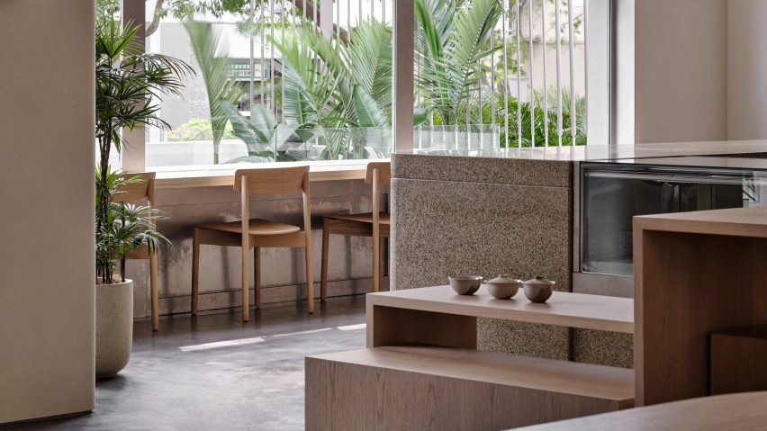 Chairs looking out at a wall of glazing next to the specked stone counter of the Basao Tea store in Xiamen, China designed by Norm Architects