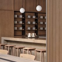 Speckled stone counter surrounded by wooden stools in interior of Basao Tea store in Xiamen, China designed by Norm Architects