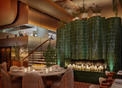 Candles stand in a fireplace clad in glossy green tiles inside a New York restaurant designed by Rockwell Group