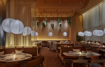 Terracotta-tiled dining room of New York restaurant designed by Rockwell Group with leather-upholstered seating booths separated by sheer curtains and illuminated by lantern-style lights
