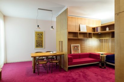 Dining table set-up next to wooden enclosure with built-in storage and seating designed by Ettore Sottsass