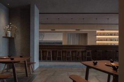 Long wooden drinks bar counter with stools on a brick plinth designed by Studio Nor