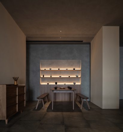 Seating nook with wooden table and benches in front of illuminated display case in restaurant interior designed by Studio Nor