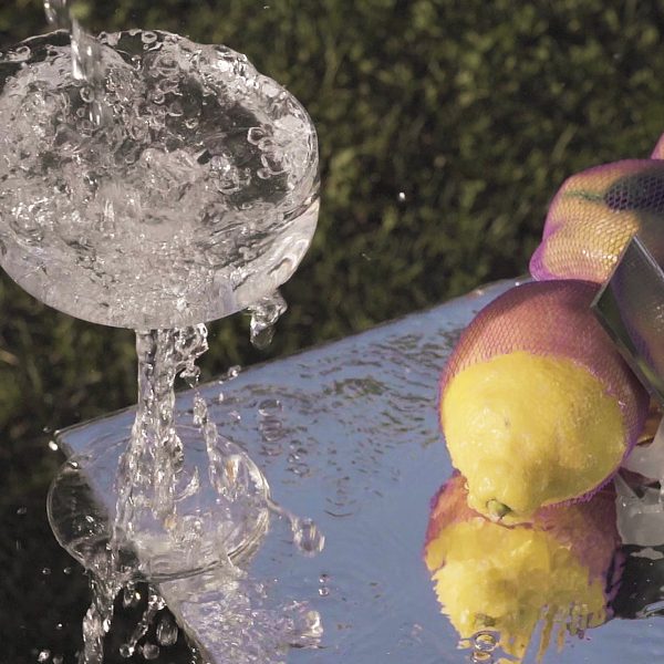 Coupe glass filled with splashing water on a reflective table with a bunch of lemons
