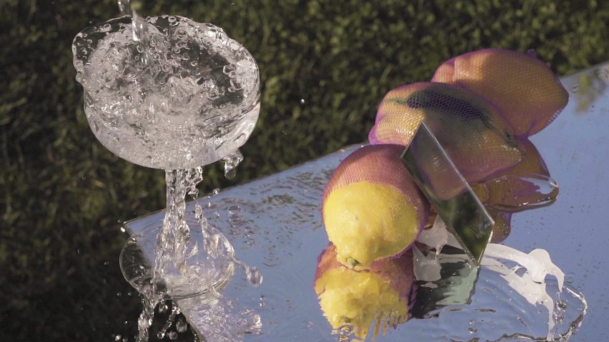 Coupe glass filled with splashing water on a reflective table with a bunch of lemons