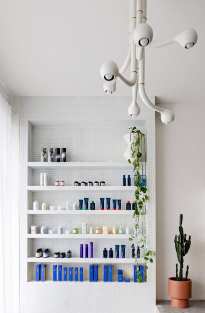 Reception area of Mitch Studio salon in Melbourne, with white-tiled custom-built retail display shelf and six-globe white chandelier by Entler