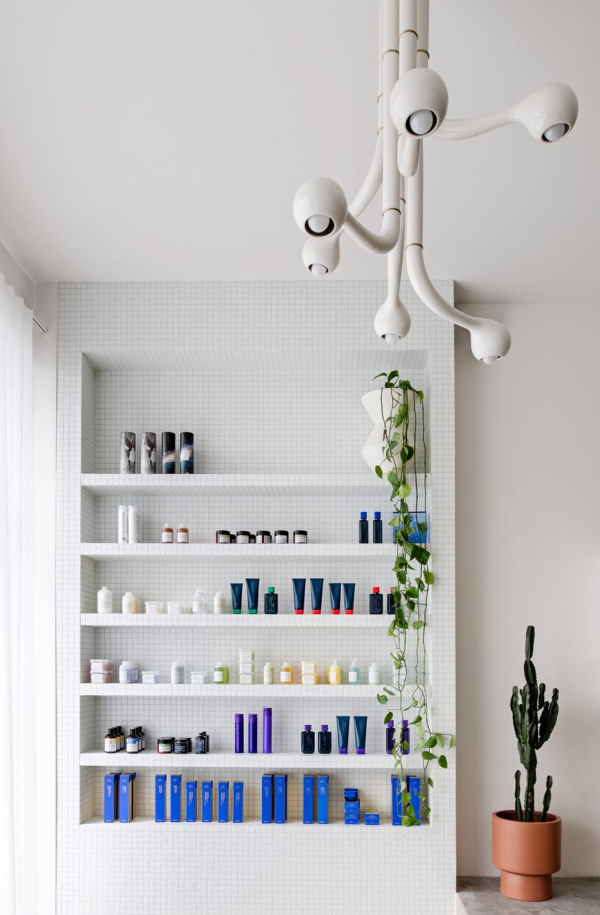 Reception area of Mitch Studio salon in Melbourne, with white-tiled custom-built retail display shelf and six-globe white chandelier by Entler