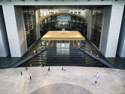 Gold-toned flat roof with apple logo capping a glazed building surrounded by tiered waterfalls