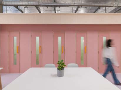 Row of phone booths with baby pink doors and orange handles in co-working office by Caro Lundin