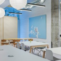Interiors of ARC Club Camberwell co-working office by Caro Lundin with large tables surrounded by chairs in front of a blue artwork