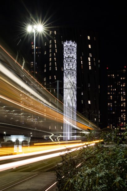 Photograph showing lit tower next to road at night