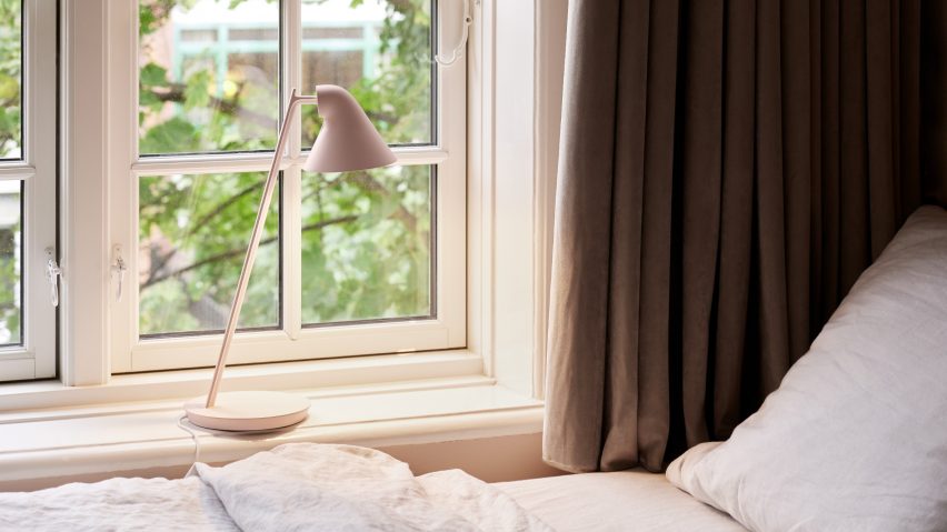 An NJP Mini table lamp by Louis Poulsen in soft pink stands on a bedroom windowsill