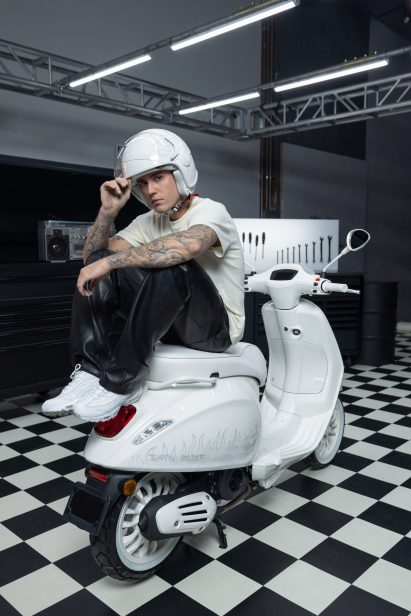 Justin Bieber in a white helmet sitting on a scooter he designed for Vespa