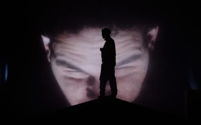 Slowthai standing in front of a video of himself
