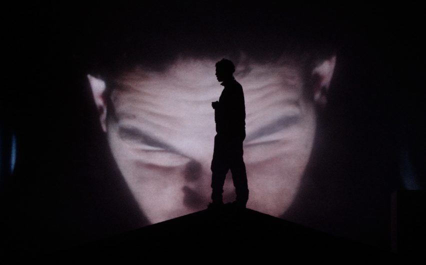 Slowthai standing in front of a video of himself