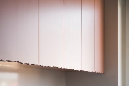 The ragged lower edge of the baby pink kitchen cupboards