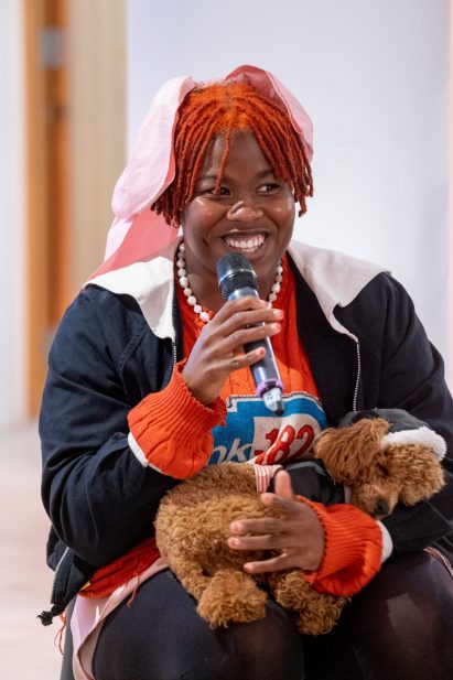 A photograph of Precious Okoyomon who is holding a small dog on their lap