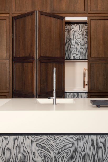 Sink in front of partially open panelled door revealing kitchenette inside