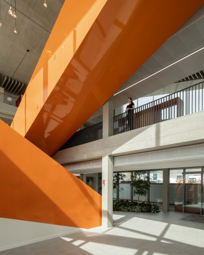 Image of a bright orange staircase crossing through a double height space at West Hub