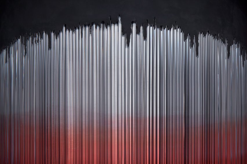 Close up of illuminated glass bars – grey above, red below, unevenly integrating with concrete at the top