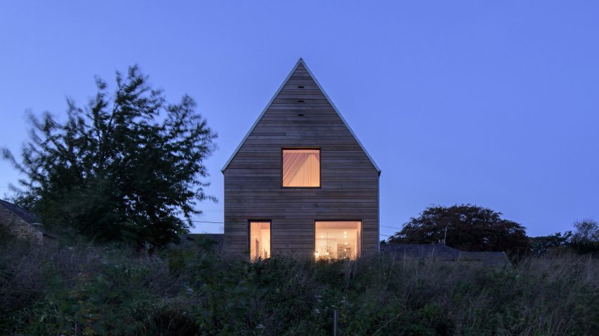 Exterior photo taken at night of North Bank house, showing steep gable and lit interior
