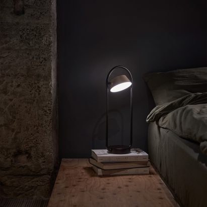 OLO table lamp in a dark painted bedroom placed on top a stack of books next to the bed