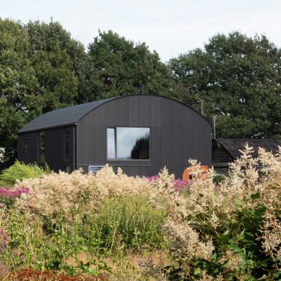 Black barrel vaulted barn in a gardened area