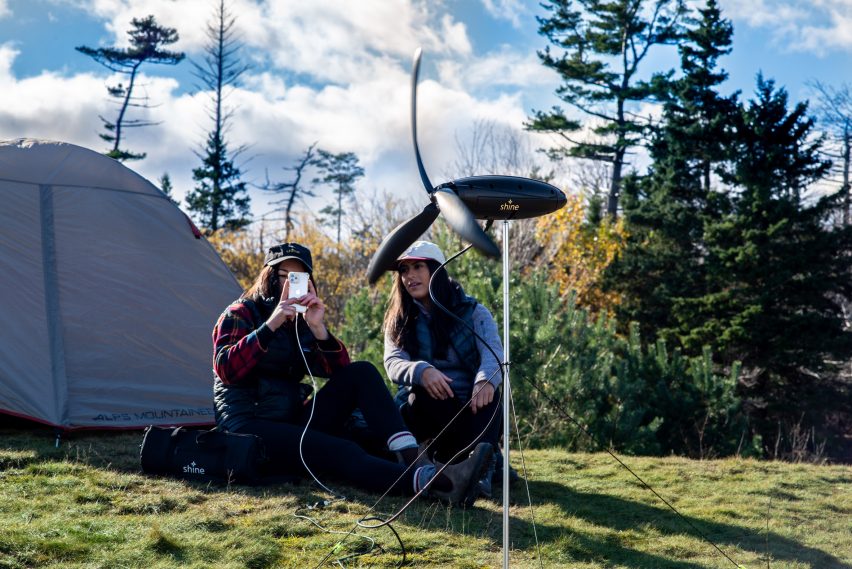 Shine Turbine set up in front of two people sitting in front of their tent in the wilderness