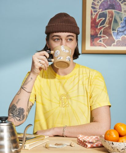 Person drinking coffee wearing a yellow PLANT dispensary Tshirt