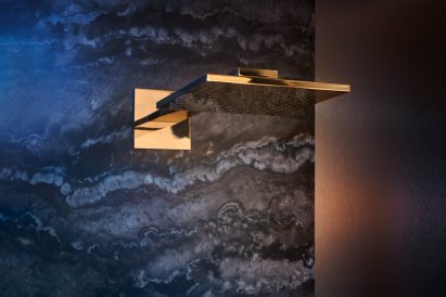 Axor polished gold optic shower head mounted on dark travertine stone