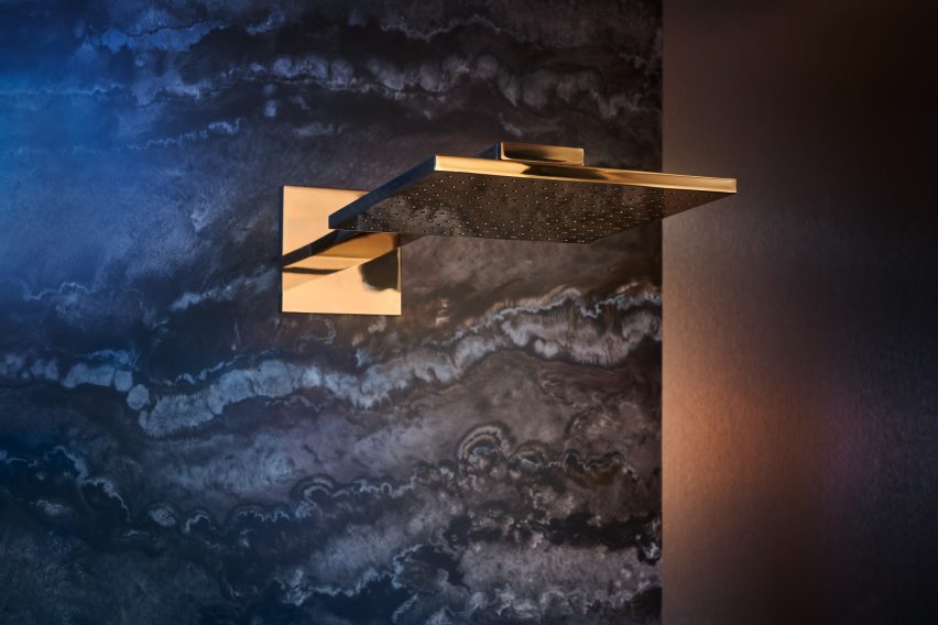 Axor polished gold optic shower head mounted on dark travertine stone